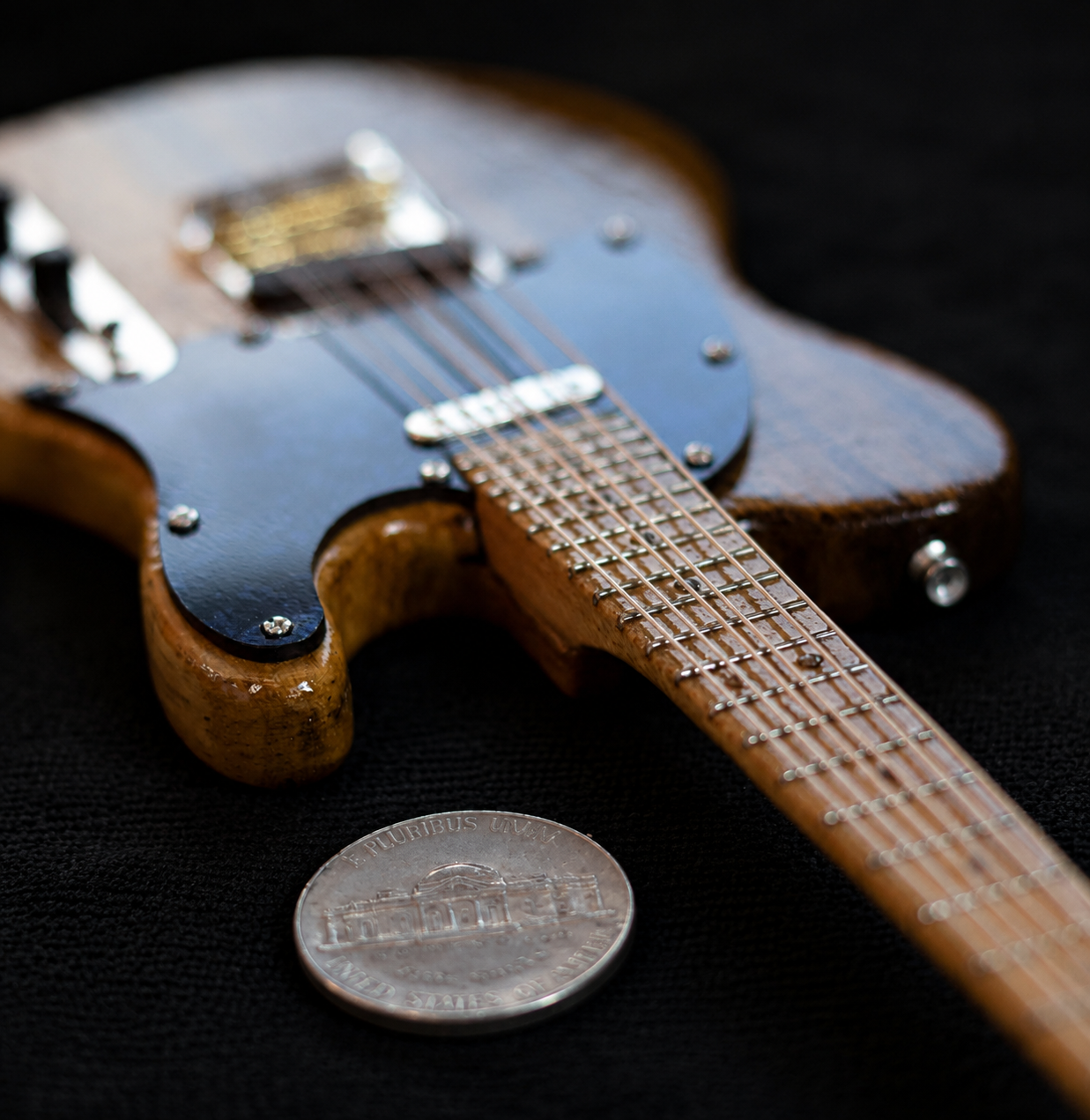 Close-up of the miniature Telecaster body and neck joint beside a US nickel for scale